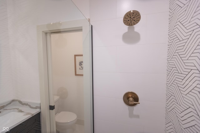 bathroom featuring a tile shower, vanity, and toilet