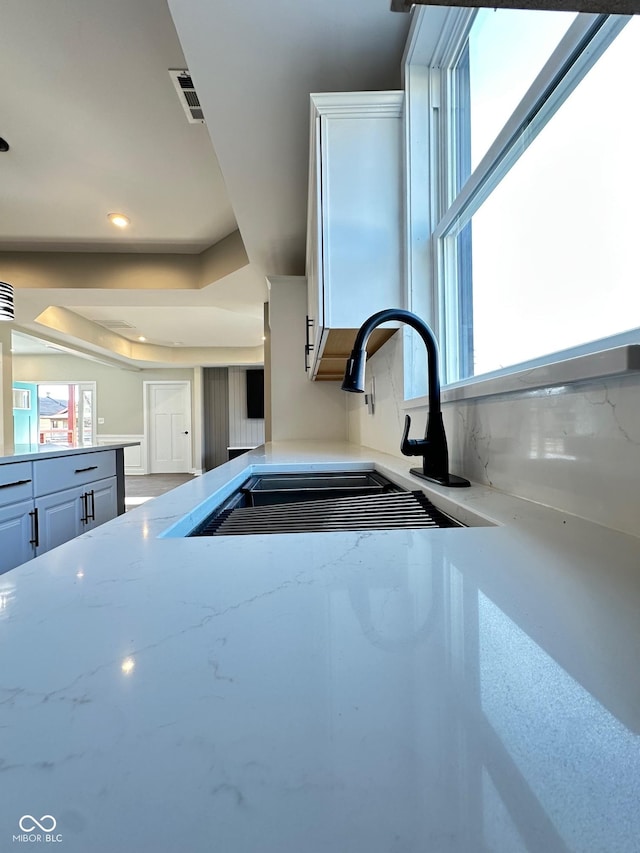 kitchen featuring a raised ceiling, white cabinetry, sink, and light stone counters