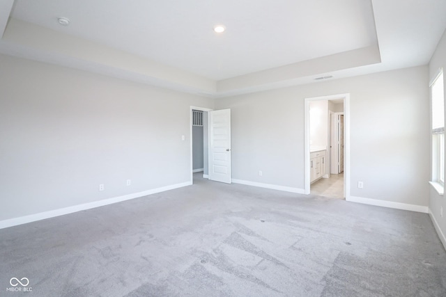 unfurnished bedroom featuring a tray ceiling, baseboards, visible vents, and light carpet