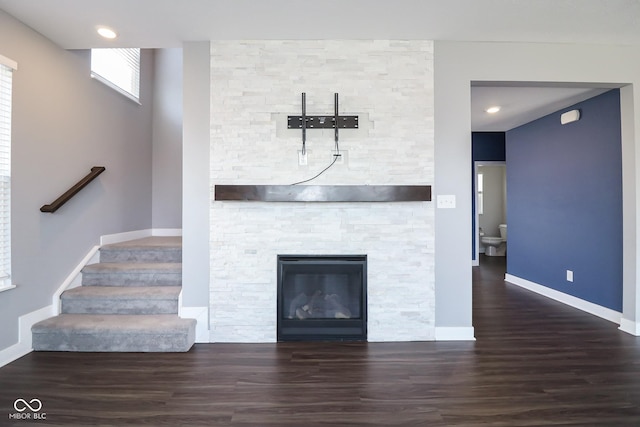 unfurnished living room featuring a stone fireplace, stairs, baseboards, and wood finished floors