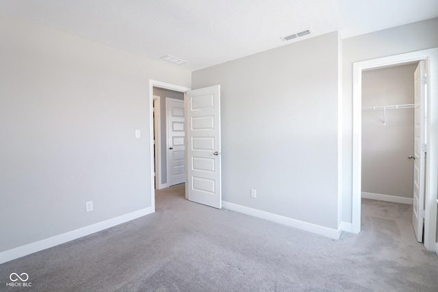 unfurnished bedroom featuring visible vents, a walk in closet, baseboards, light colored carpet, and a closet