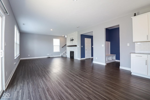 unfurnished living room featuring baseboards, a fireplace, and dark wood-style flooring