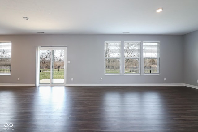 unfurnished room featuring baseboards, dark wood-style flooring, and a wealth of natural light