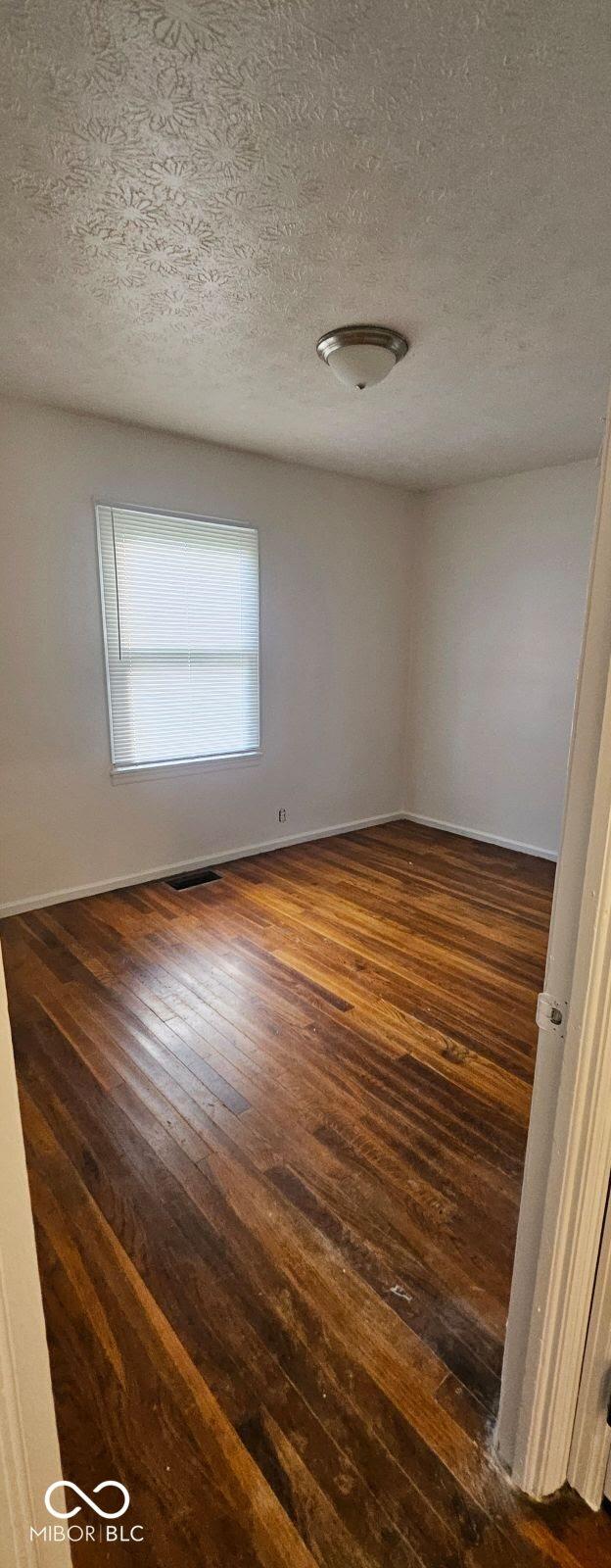 unfurnished room with a textured ceiling, dark wood finished floors, visible vents, and baseboards