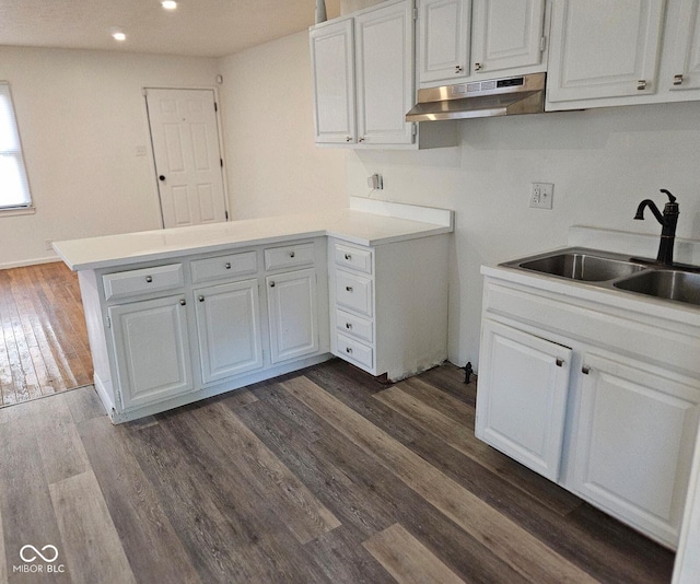 kitchen featuring under cabinet range hood, a peninsula, a sink, white cabinetry, and light countertops