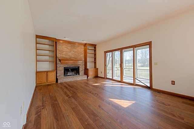 unfurnished living room with a brick fireplace, dark hardwood / wood-style floors, and built in shelves