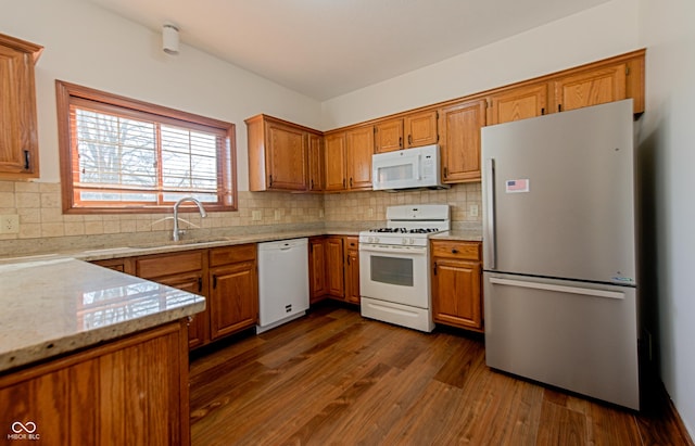 kitchen with sink, dark hardwood / wood-style flooring, white appliances, light stone countertops, and backsplash