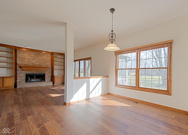 unfurnished living room featuring a brick fireplace, hardwood / wood-style floors, and built in shelves