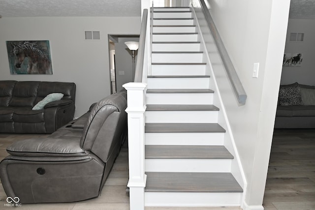 stairs with wood-type flooring and a textured ceiling