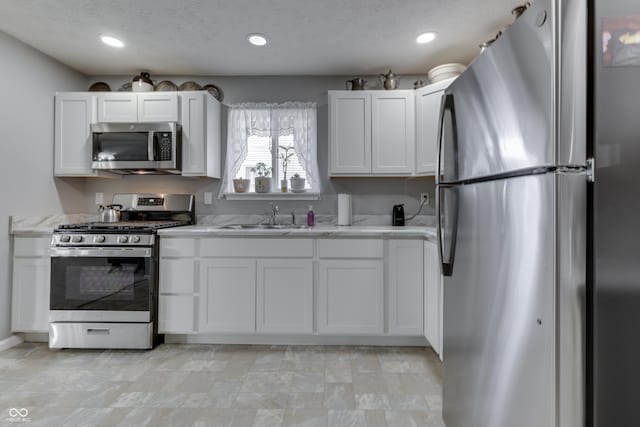 kitchen featuring stainless steel appliances, white cabinetry, sink, and a textured ceiling