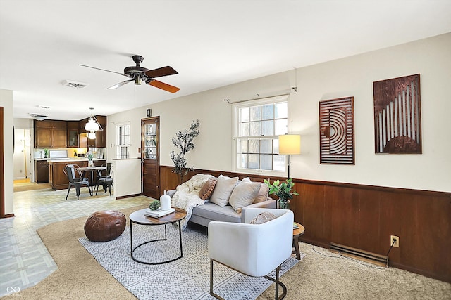 living room featuring a ceiling fan, a wainscoted wall, wood walls, and visible vents