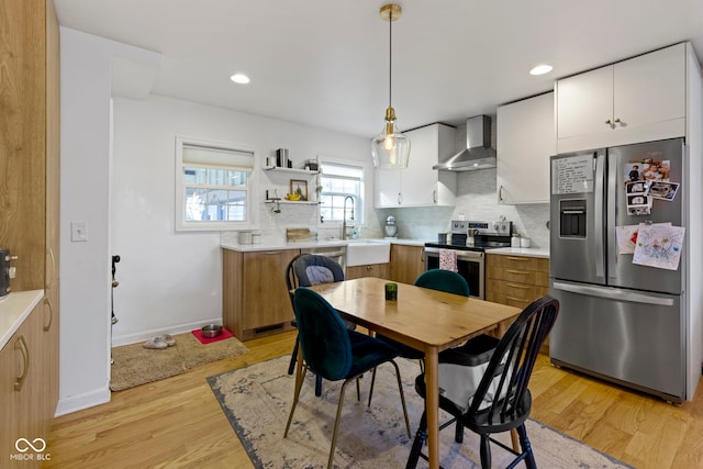 kitchen featuring wall chimney exhaust hood, sink, white cabinetry, appliances with stainless steel finishes, and pendant lighting