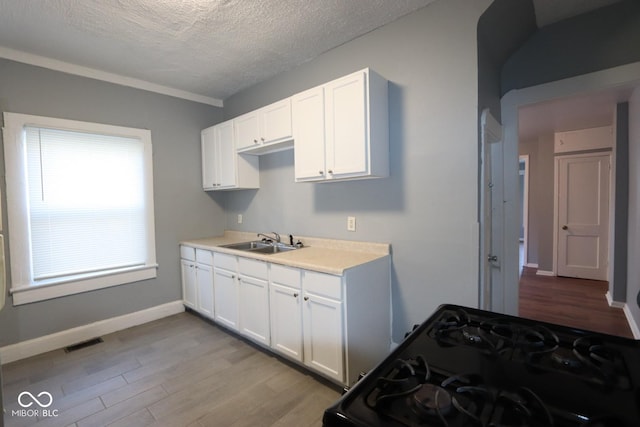 kitchen featuring black gas range oven, sink, white cabinetry, and light wood-type flooring