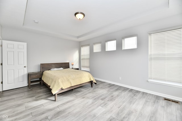 bedroom with light hardwood / wood-style floors and a tray ceiling