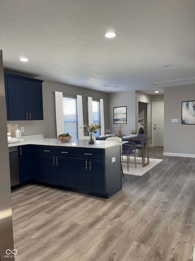 kitchen featuring blue cabinets, washer / dryer, kitchen peninsula, and light wood-type flooring