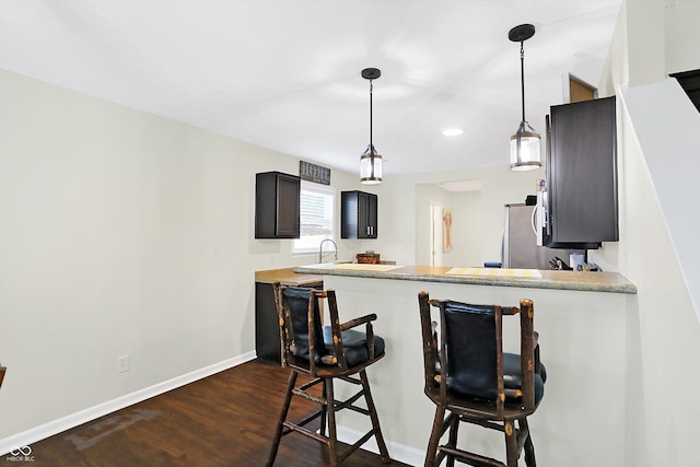 kitchen with a breakfast bar area, stainless steel fridge, dark hardwood / wood-style flooring, kitchen peninsula, and pendant lighting