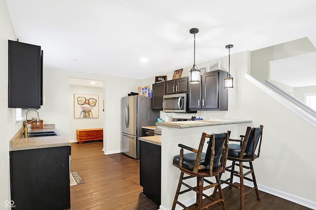 kitchen with appliances with stainless steel finishes, a breakfast bar, sink, dark hardwood / wood-style flooring, and kitchen peninsula