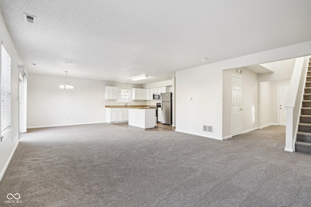 unfurnished living room with an inviting chandelier, sink, carpet floors, and a textured ceiling