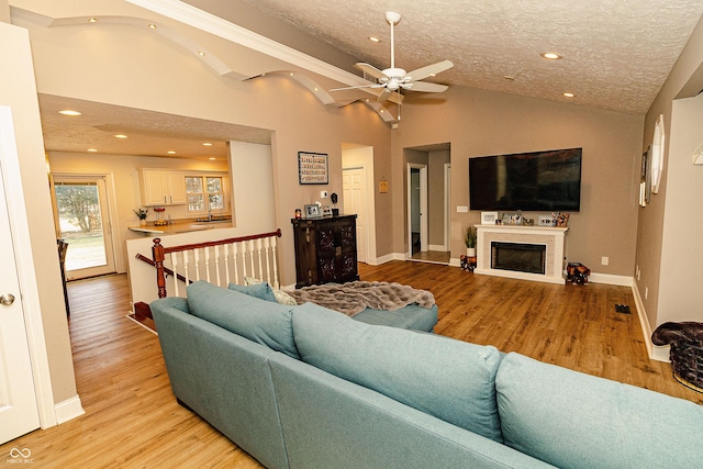 living room featuring a fireplace, lofted ceiling, sink, a textured ceiling, and light hardwood / wood-style flooring