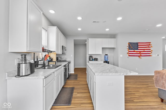 kitchen featuring sink, a kitchen island, stainless steel appliances, light hardwood / wood-style floors, and white cabinets