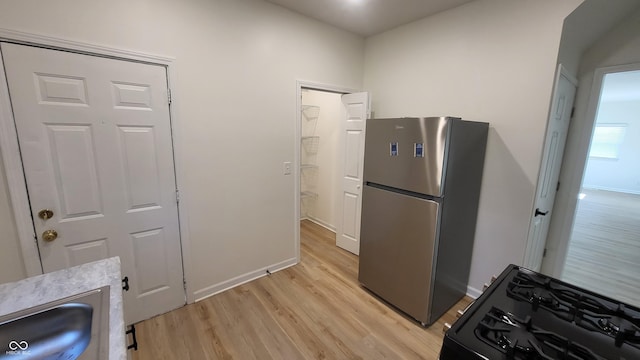 kitchen featuring black gas stove, stainless steel fridge, and light hardwood / wood-style flooring