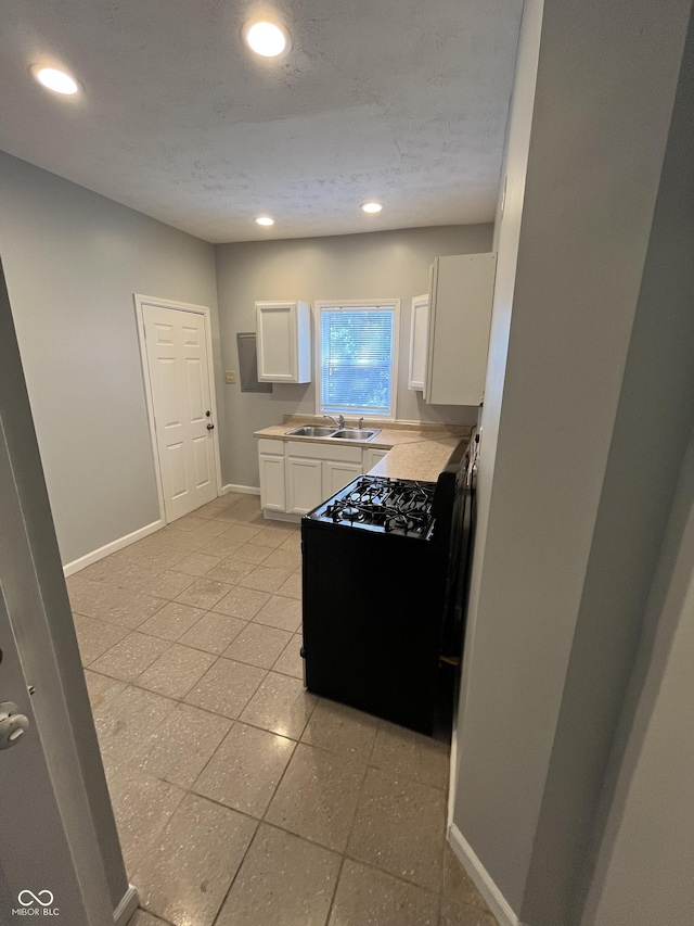 kitchen with sink, white cabinets, a textured ceiling, and black gas range