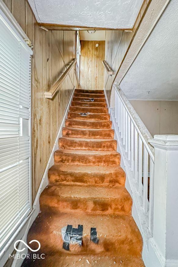 stairs with wooden walls and a textured ceiling