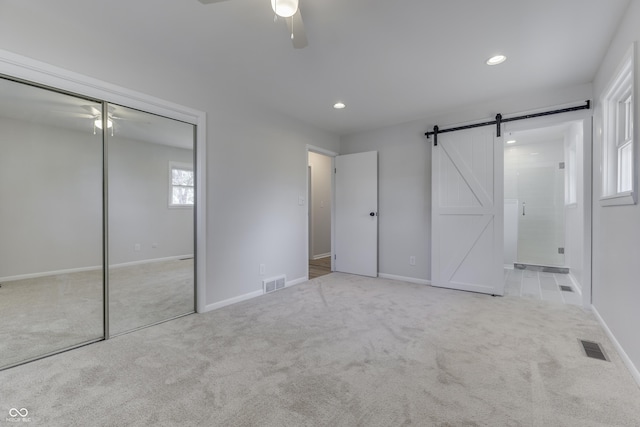 unfurnished bedroom with a barn door, light carpet, ceiling fan, and a closet