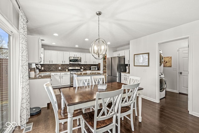 dining room with dark wood-type flooring, stacked washer and dryer, sink, and a notable chandelier