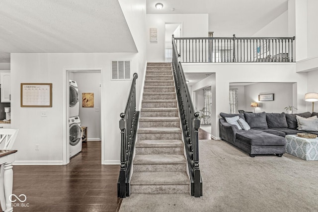 stairs featuring hardwood / wood-style flooring, stacked washing maching and dryer, and a towering ceiling