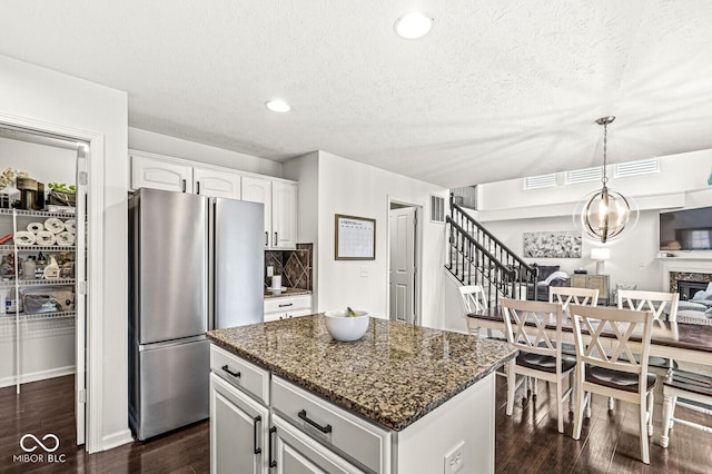 kitchen featuring white cabinetry, hanging light fixtures, dark stone countertops, stainless steel refrigerator, and a kitchen island