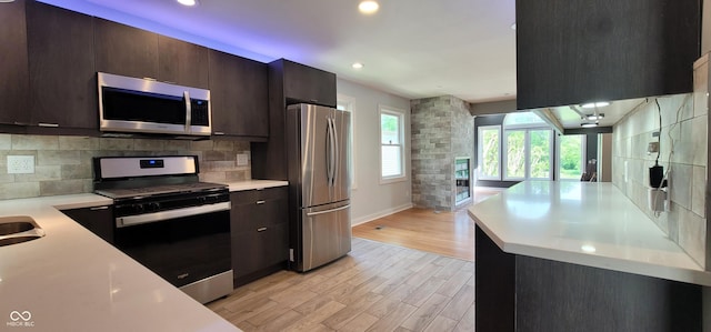 kitchen with stainless steel appliances, dark brown cabinetry, light hardwood / wood-style floors, decorative backsplash, and kitchen peninsula