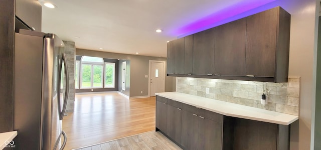 kitchen featuring dark brown cabinetry, light wood-type flooring, backsplash, and stainless steel refrigerator