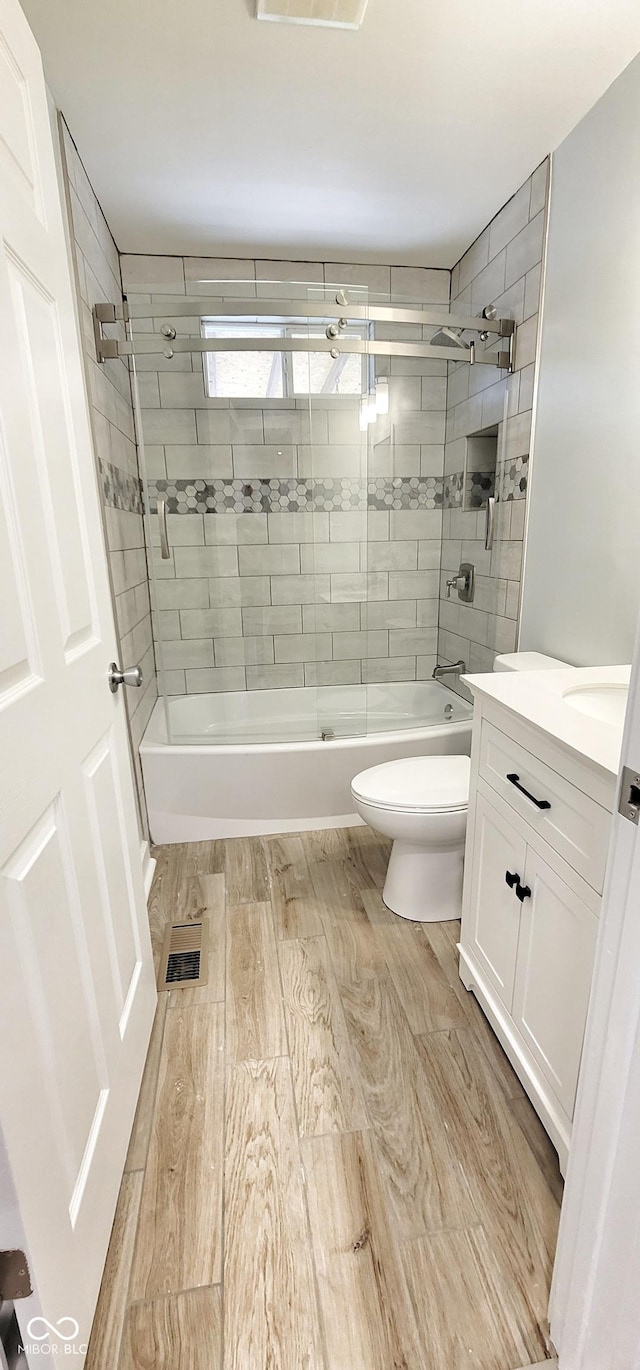 full bathroom featuring hardwood / wood-style flooring, vanity, combined bath / shower with glass door, and toilet