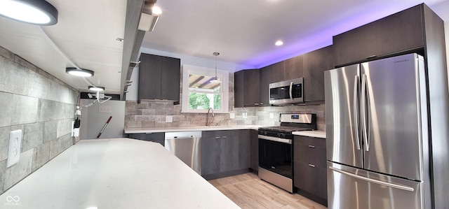 kitchen with stainless steel appliances, pendant lighting, backsplash, and light hardwood / wood-style flooring