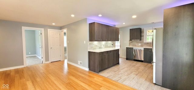 kitchen featuring dark brown cabinetry, tasteful backsplash, decorative light fixtures, light hardwood / wood-style flooring, and appliances with stainless steel finishes