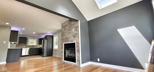 unfurnished living room with a fireplace, sink, a skylight, and light hardwood / wood-style floors