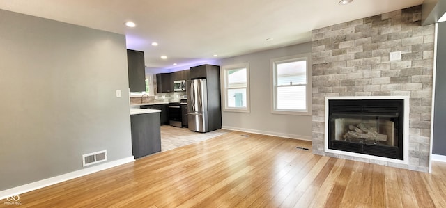 kitchen featuring a large fireplace, backsplash, dark brown cabinetry, stainless steel appliances, and light wood-type flooring