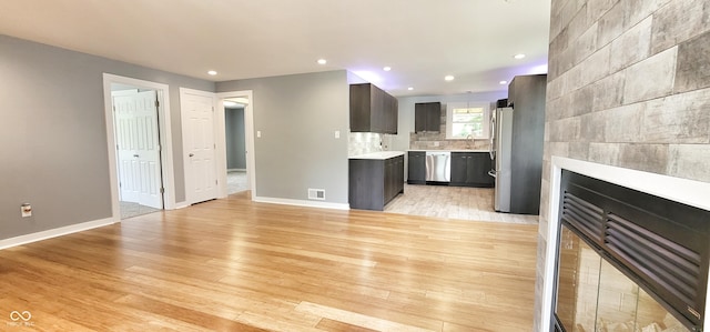 kitchen with stainless steel appliances, tasteful backsplash, dark brown cabinets, and light hardwood / wood-style flooring