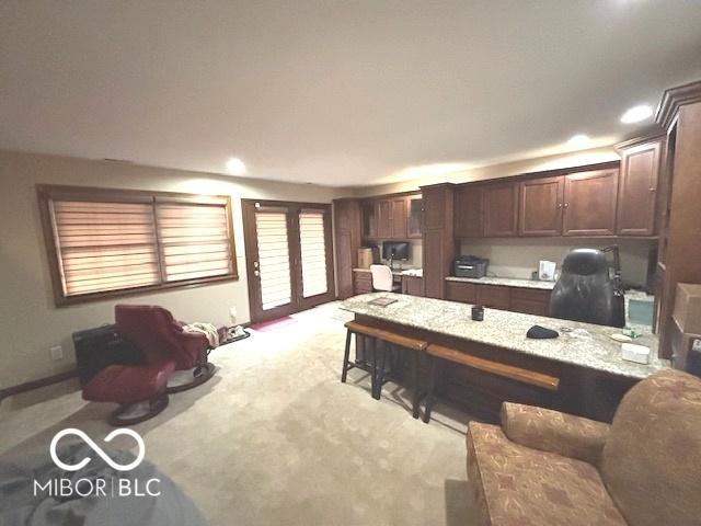 kitchen with light carpet, light stone counters, and dark brown cabinets