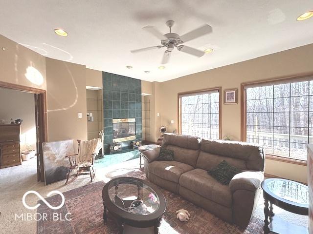 living room with a tiled fireplace, carpet floors, and ceiling fan