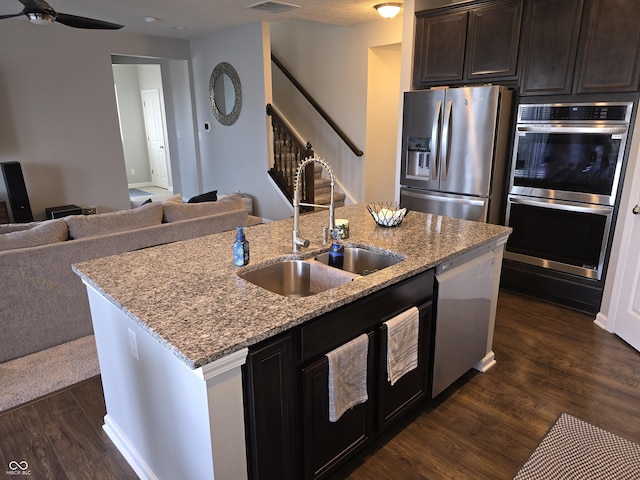 kitchen featuring dark brown cabinetry, sink, appliances with stainless steel finishes, dark hardwood / wood-style floors, and an island with sink