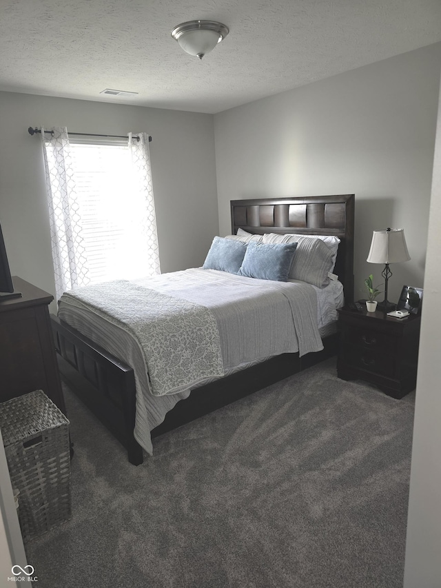 bedroom with a textured ceiling and dark colored carpet