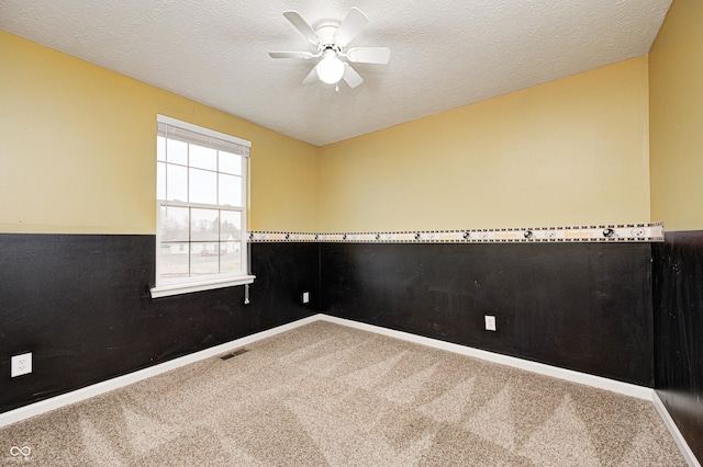 carpeted empty room with ceiling fan, a textured ceiling, a wainscoted wall, wood walls, and visible vents