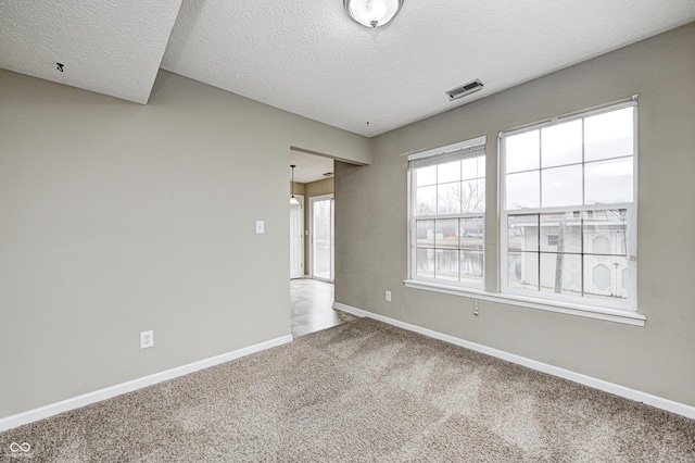 empty room with a textured ceiling, carpet flooring, visible vents, and baseboards