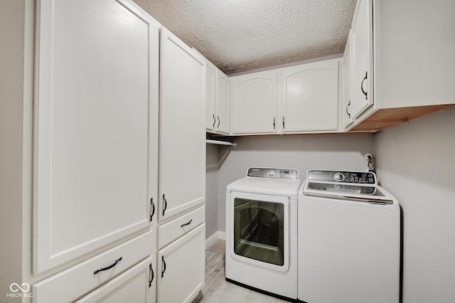 laundry area featuring cabinets, light wood-type flooring, washing machine and clothes dryer, and a textured ceiling