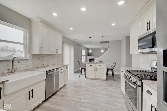 kitchen featuring sink, hanging light fixtures, light hardwood / wood-style flooring, stainless steel appliances, and light stone countertops