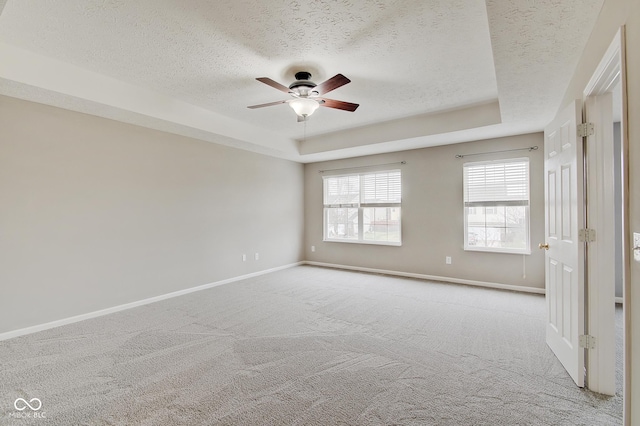 unfurnished room featuring ceiling fan, light colored carpet, a textured ceiling, and a tray ceiling