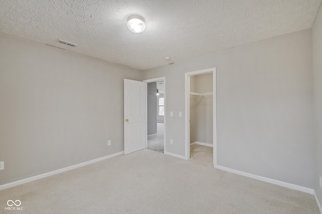 unfurnished bedroom featuring a spacious closet, light carpet, a textured ceiling, and a closet