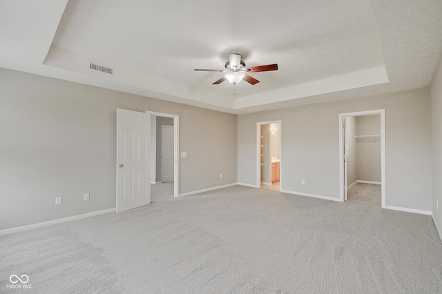 unfurnished bedroom featuring a walk in closet, a tray ceiling, light colored carpet, and a textured ceiling